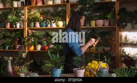 Side-view portrait of successful male caucasian florist using tablet online buying flowers for florist shop. Beautiful professional man worker with Stock Photo
