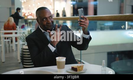 Mature African American business man with mobile phone take picture selfie photo in cafe with coffee tea and tasty cake middle-aged businessman male Stock Photo