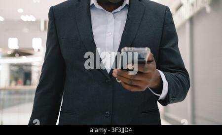 Cropped view unrecognizable African American middle-aged business man with mobile phone walking in shopping mall. Cropped view unknown businessman Stock Photo