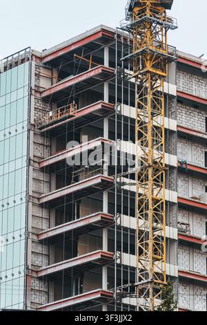 Contemporary urban construction site showing unfinished multi storey building with tower crane, concrete structure, steel framework and exterior facad Stock Photo