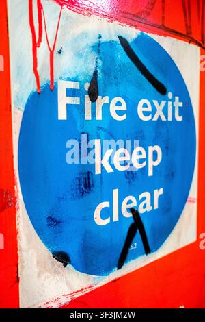 London UK, July24 2026, Close-Up Of A Vandalised Blue Circle Fire Exit Keep Clear Sign With Graffiti Tags On A White Background, UK Stock Photo