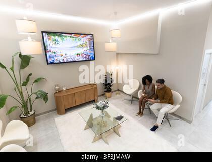 Two diverse people sitting in a professional waiting room, using a digital tablet Stock Photo