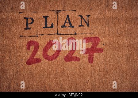 Close up shot words PLAN 2027 in black stamp and red marker on textured brown cardboard Stock Photo