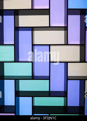 Vertical shot of modern geometric wall shelf with colorful neon backlit panels in purple blue and teal abstract interior design background. Stock Photo