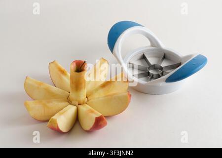 Sliced red apple arranged in flower shape next to blue apple cutter on white background Stock Photo