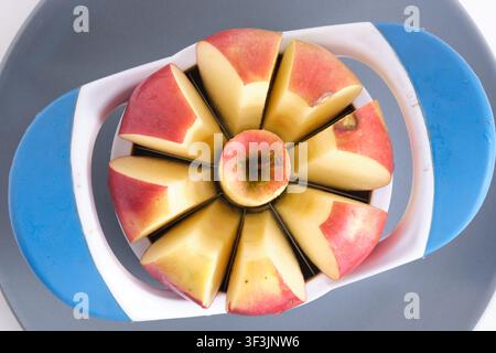 Top view close up red apple being sliced with blue plastic apple corer slicer tool Stock Photo
