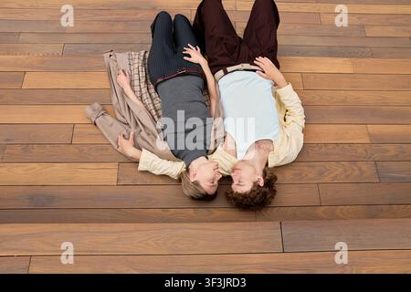 Young couple in fall outfits lying on wooden steps and looking at each other, top view Stock Photo
