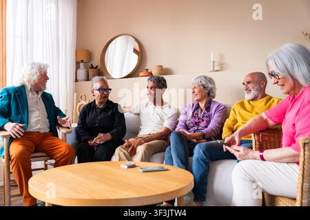 Group of happy multicultural senior friends gathering and talking in living room, sharing moments of joy and connection while experiencing active agin Stock Photo