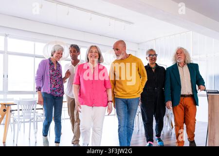 Group of diverse senior friends smiling while walking together indoors, enjoying each other's company and experiencing happiness and community Stock Photo