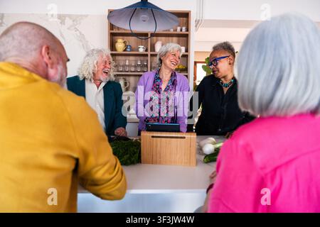 Group of diverse senior friends enjoying a lively kitchen conversation, preparing a meal while laughing, sharing friendship, and experiencing an activ Stock Photo
