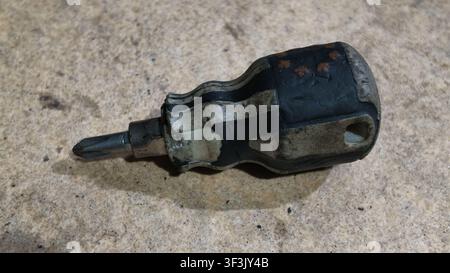 Close-up of a mini precision screwdriver with a worn handle placed on a textured concrete surface. Suitable for DIY, repair, maintenance, and tool-rel Stock Photo