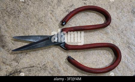Close-up of vintage red-handled scissors placed on a textured concrete surface, suitable for concepts related to tools, craftsmanship Stock Photo