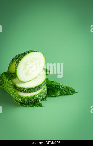 Organic zucchini slices with fresh leaves on pastel green background . Stock Photo