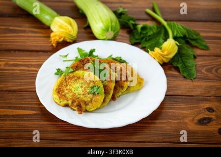 Fresh vegetable zucchini pancakes on white plate with rustic wooden background . Stock Photo