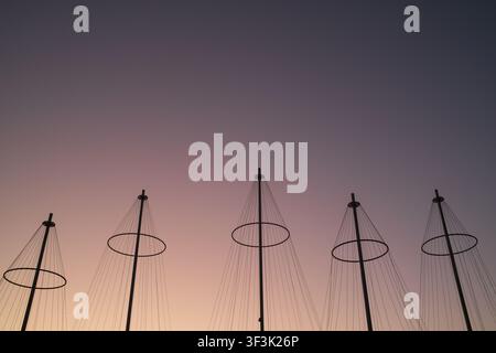 View of the sculptural masts of the Cirkelbroen bridge silhouetted against a vibrant sunset sky in Copenhagen, Denmark. Stock Photo