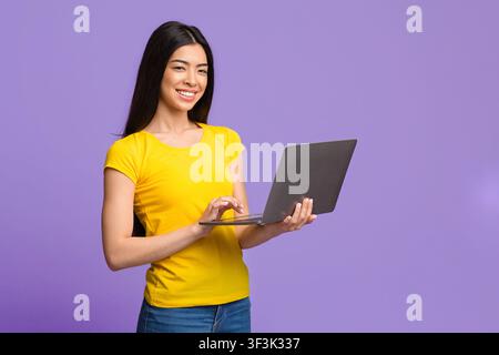 Positive Young Asian Woman Posing With Laptop Computer Over Purple Background Stock Photo