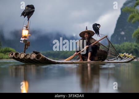 Guilin, Guangxi, China - 18 June 2026: View of a traditional cormorant fisherman on a bamboo raft with his birds and a lantern, set against the misty Stock Photo