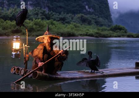 Guilin, Guangxi, China - 18 June 2026: View of a traditional cormorant fisherman on a bamboo raft near Xingpingzhen with a glowing lantern and cormora Stock Photo