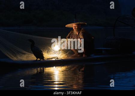 Guilin, Guangxi, China - 18 June 2026: View of a traditional cormorant fisherman with a lantern and fishing net on a bamboo raft at night in Xingpingz Stock Photo
