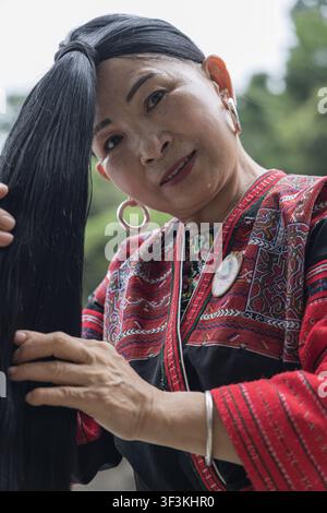 Guangxi, China - 18 June 2026: View of a Red Yao woman with exceptionally long black hair, wearing traditional red and black embroidered clothing and Stock Photo