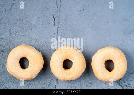 Flat lay shot of three classic sugar donuts lined up on a gray concrete surface with copy space for design Stock Photo