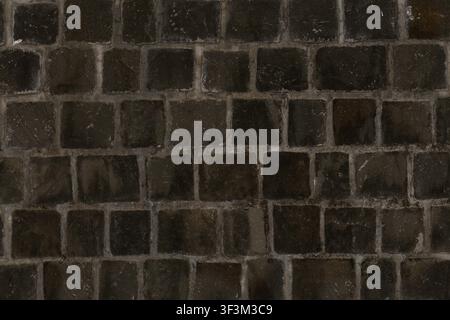 A wall composed of dark charcoal square stone blocks, creating a uniform and modern architectural look. Stock Photo