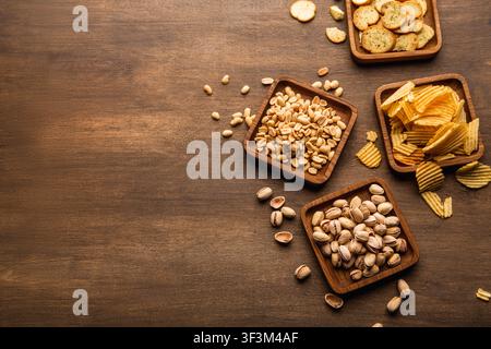 Crispy snacks on background. Pistachios, nuts, crisps and chips in plate and scattered on table Stock Photo