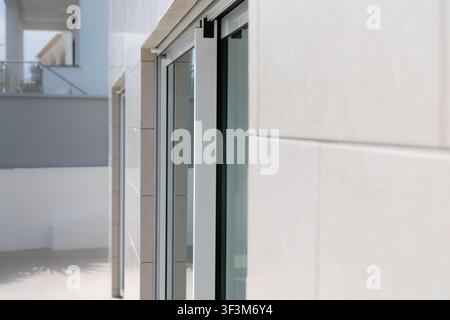 Exterior view of a contemporary building featuring sleek sliding glass doors and textured beige stone cladding Stock Photo