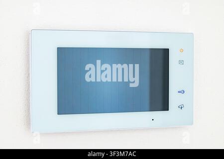 A sleek, white intercom panel mounted on a textured wall, featuring a digital display and intuitive control icons for enhanced home security and acces Stock Photo