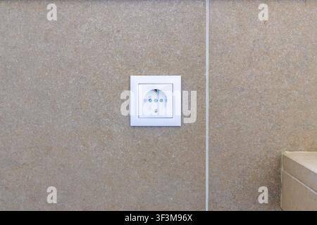 A single white electrical outlet is centered on a neutral-toned wall with a subtle speckled pattern, suggesting a clean and contemporary interior desi Stock Photo