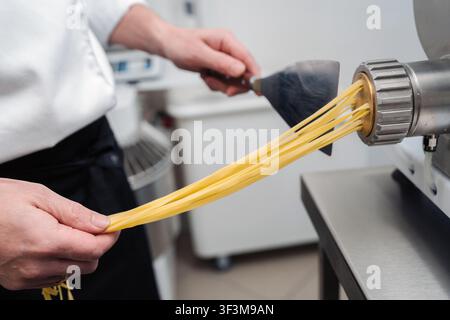 Chef preparing fresh pasta using a machine in a kitchen setting during the day Stock Photo