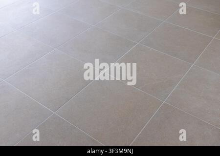 A close-up view of a tiled floor featuring large, square tiles in a neutral beige color with a slightly textured surface Stock Photo