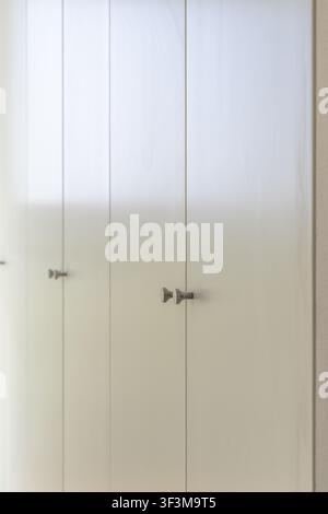 A clean and modern interior design featuring a series of seamless white cabinet doors with small, geometric hardware Stock Photo