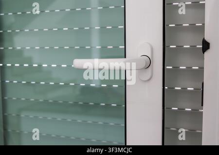 Close-up view of a white window handle on a modern building, showing roller shutters behind the glass Stock Photo
