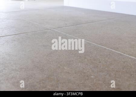 A close-up view of a contemporary beige tiled floor, showcasing its texture and precise grout lines illuminated by gentle ambient light Stock Photo
