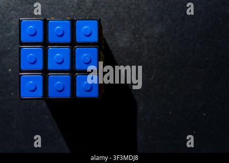 Blue plastic blocks form a cube against dark surface. Shadow falls sharply beside the structure. Minimalist design invites curiosity and creativity. P Stock Photo