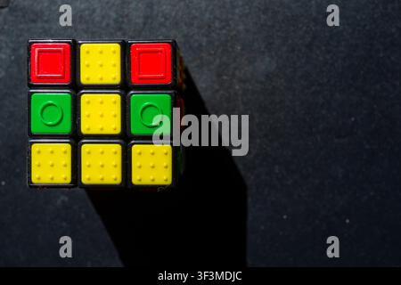 Colorful cube rests on dark surface. Shadows add depth and contrast. Bright hues stand out against deep background. Ideal for games, puzzles, or creat Stock Photo