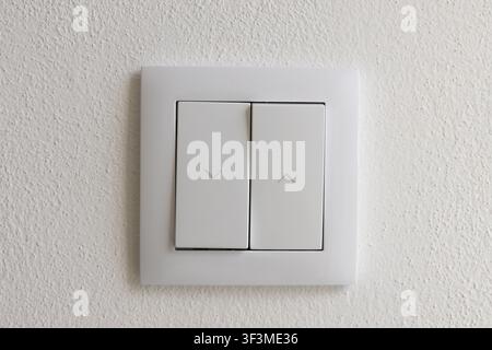 A close-up view of a contemporary white wall switch featuring two buttons, each marked with an arrow indicating direction Stock Photo