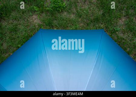 Blue umbrella rests on grassy ground. Soft tones radiate from its curved canopy. Green grass surrounds the sheltering cover. Perfect for outdoor cover Stock Photo