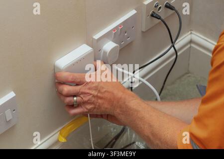 Telecoms engineer in hi-vis top connecting SC APC green fibre optic cable into wall-mounted optical network terminal during residential full fibre bro Stock Photo