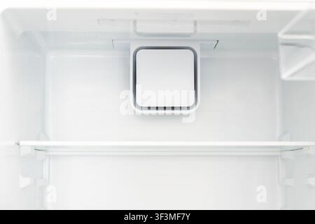 A bright, sterile view inside an empty refrigerator compartment showing a shelf and a square air circulation vent Stock Photo