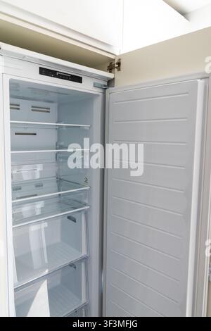 An empty, clean, white upright freezer is shown with its door ajar, revealing multiple glass shelves and transparent drawers inside Stock Photo
