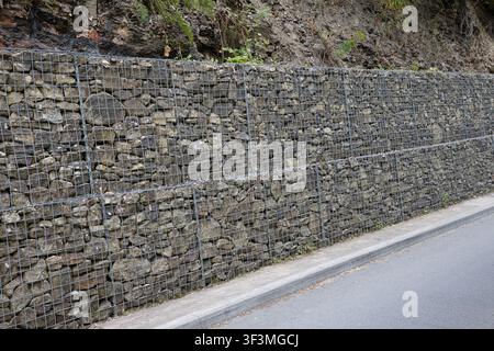 Gabion retaining wall constructed with wire mesh baskets filled with grey rocks, supporting an earthen embankment, Healey Dell, Rochdale, UK. Stock Photo