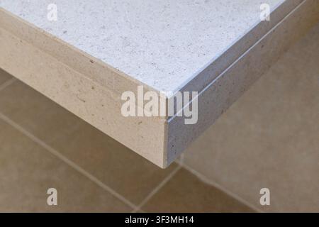 A detailed view of a light-colored stone surface and its layered edge, highlighting the material's granular texture and clean lines Stock Photo