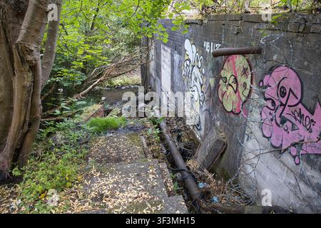 Concrete outdoor stairwell and drainage pipe system covered in graffiti alongside the river Spodden on Woodland Road, Rochdale, UK. Stock Photo