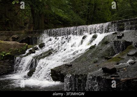 Water cascading over wide stone weir located directly under the Healey Dell railway viaduct on the River Spodden in Rochdale, UK. Stock Photo