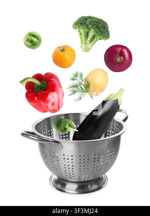 Different fresh vegetables falling into colander on white background Stock Photo
