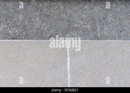 A detailed view showcases the contrasting textures of rough aggregate concrete meeting clean, light-colored stone tiles with grout lines Stock Photo