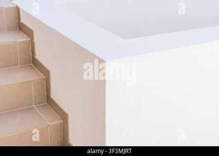 A close-up view showcases the textured surface of a white architectural element adjacent to a set of neutral-toned tiled stairs Stock Photo