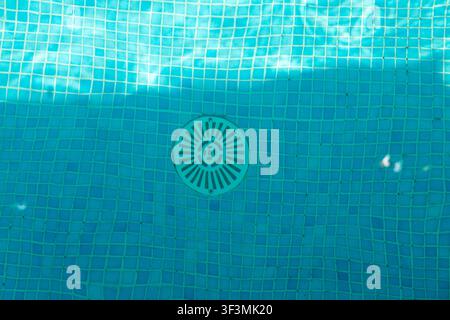 A close-up perspective of the submerged floor of a swimming pool, showcasing the blue mosaic tiles and a circular drain grate Stock Photo